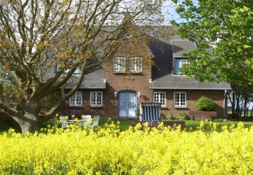 a large brick house with a tree and yellow flowers at Haus Wolfram App Gondeline Morsumer Kliff in Archsum