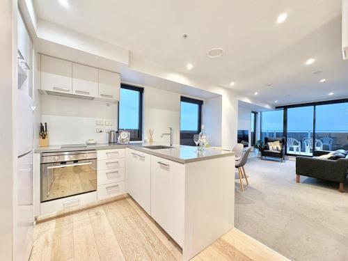 a kitchen with white cabinets and a living room at Sky Tower Views High-Floor Apt Pool Gym Access in Auckland