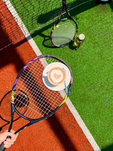 a person holding a cup of coffee on a tennis court at Mona Hotel and Cottages in Lankaran