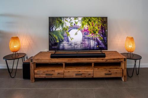 a tv on top of a wooden entertainment center with two lamps at Luxury Oceanview Escape in Nelly Bay