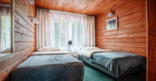 two beds in a room with wooden walls and a window at Ośrodek Wypoczynkowy Kołatek in Olsztynek