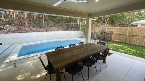a patio with a wooden table and a swimming pool at New Pool Now Open! - Trinity Beach Haven - Luxury 4 bedroom home, Steps to the Beach, Surrounded by Mountains in Trinity Beach