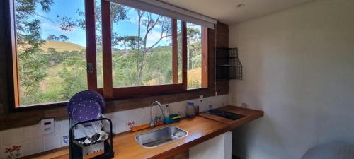 a kitchen counter with a sink and two windows at Recanto na Mantiqueira - Casa 3Q a 2 km do centro in Gonçalves