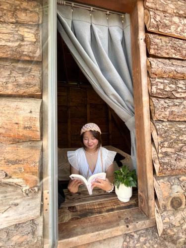 a woman sitting in a window reading a book at Nhà Tĩnh - Tiệm Cà phê Tĩnh 2 in Ấp Ða Lợi