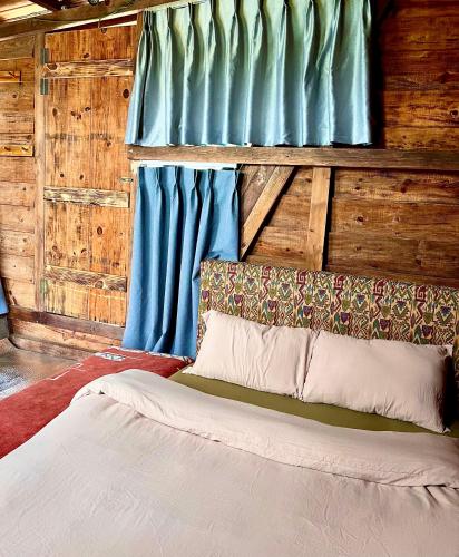 a bed in a room with wooden walls and blue curtains at Nhà Tĩnh - Tiệm Cà phê Tĩnh 2 in Ấp Ða Lợi