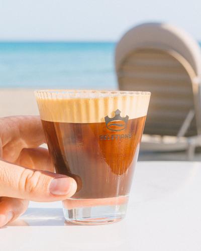 a hand holding a cup of coffee in front of the beach at Artemis in Makry Gialos