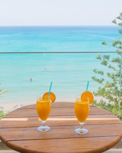 two glasses of orange juice sitting on a table overlooking the beach at Artemis in Makry Gialos
