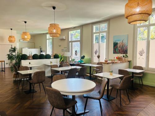 un restaurant avec des tables, des chaises et des fenêtres dans l'établissement Hotel De Ma Tante, à Lamalou-les-Bains
