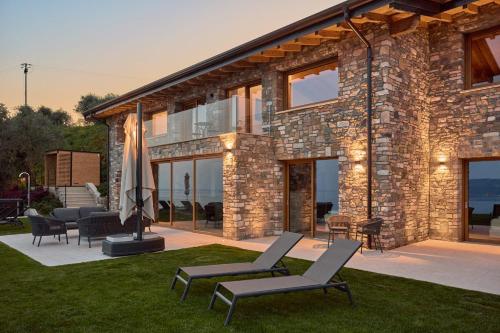 a stone house with lounge chairs and an umbrella at Colago Private Villas Lake Garda in Toscolano Maderno