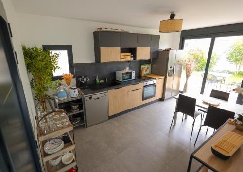 une cuisine avec des appareils en acier inoxydable, une table et des chaises dans l'établissement Logement cosy neuf avec jardin, à Mions