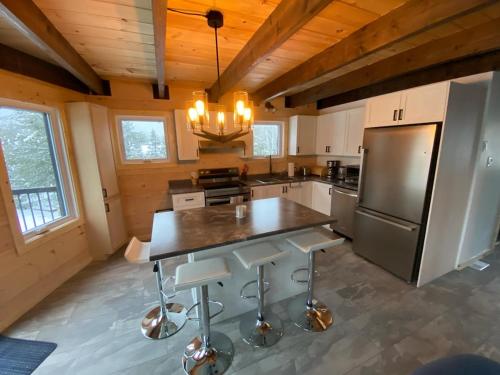 eine Küche mit Kühlschrank und einem Tisch mit Hockern in der Unterkunft Chalet au coeur des montagnes in LʼAnse-Saint-Jean