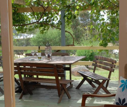 una mesa de madera y sillas en un porche con mesa y 2 sillas en Twisted Gum Vineyard Cottage, en Ballandean