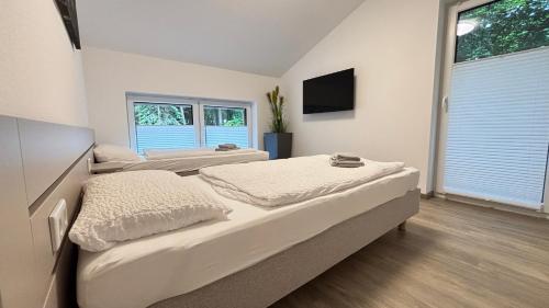 two beds in a room with a tv on the wall at Modernes Ferienhaus am See mit Garten in Wiefelstede
