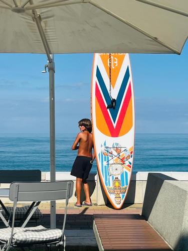 a man standing next to a surfboard on the beach at Pitna Guest House in K'obulet'i
