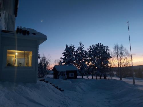 a house covered in snow next to a building at Rooms in a big wooden home, kotimajoitus, homestay in Muonio