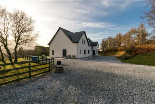 a white house with a black roof on a gravel road at MacGregor Ranch Apartment in Spean Bridge