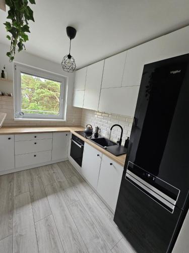 Una cocina con gabinetes blancos y un refrigerador negro. en Apartament z widokiem na las, en Ustka