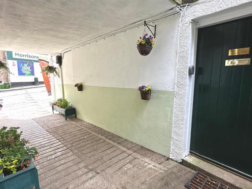 a green door with a basket of flowers on a wall at The Canongate Coorie in Jedburgh