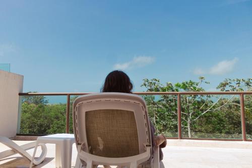 a person sitting in a chair on a balcony looking at the view at Apartamento Flamingo - Santuario Apartments in Chemuyil