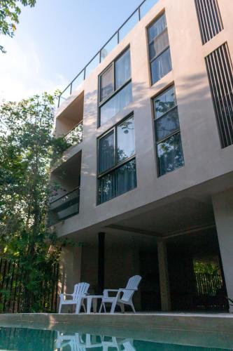 a building with two white chairs and a swimming pool at Apartamento Flamingo - Santuario Apartments in Chemuyil