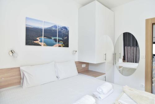 a white bedroom with a bed and a mirror at Apartments A Čanj in Čanj