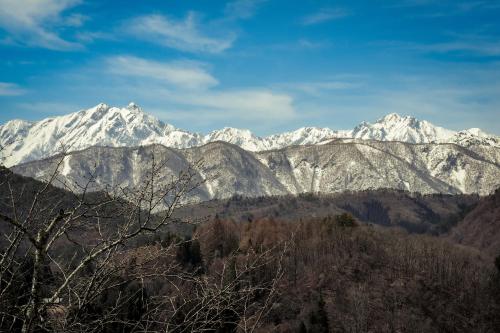 a snow covered mountain range with trees in the foreground at Yamabo inn 古民家 Traditional Japanese Home in Omachi