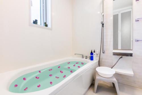 a white bathroom with a tub and a toilet at Kahoo House in Nago