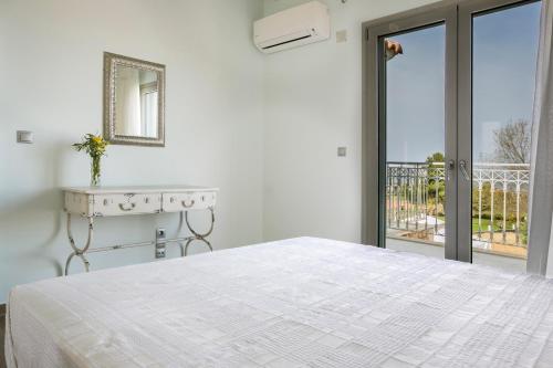 a white bedroom with a bed and a balcony at Afrodite Luxury Villa in Svoronata