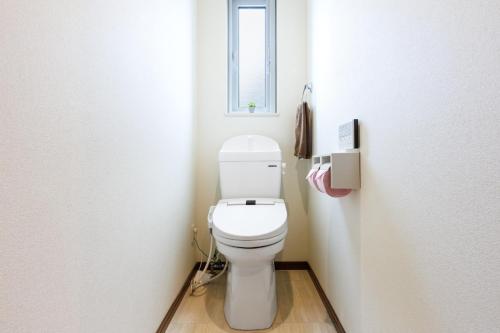 a bathroom with a white toilet with a window at Kahoo House in Nago