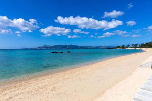 a beach with the ocean and blue sky and clouds at Kahoo House in Nago