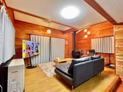 a living room with a black leather couch and a television at 花の街1079# Nature Escape BBQ in Tsumagoi
