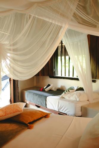 a bedroom with two beds with white drapes at Aldeia Setemares Bangalôs - Praia do Sargi - Serra Grande in Serra Grande