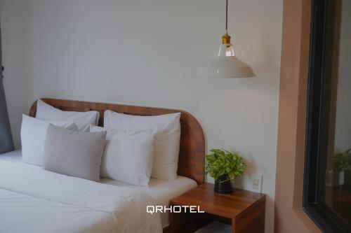a bed with white pillows and a table with a plant at QR Hotel Dalat in Xuan An