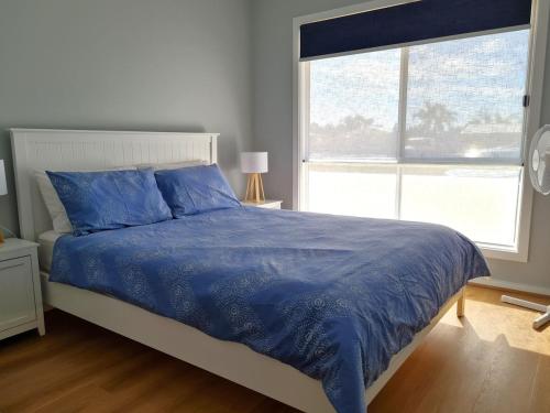 a bedroom with a bed with a blue comforter and a window at Sun of a Beach in Port Moonta