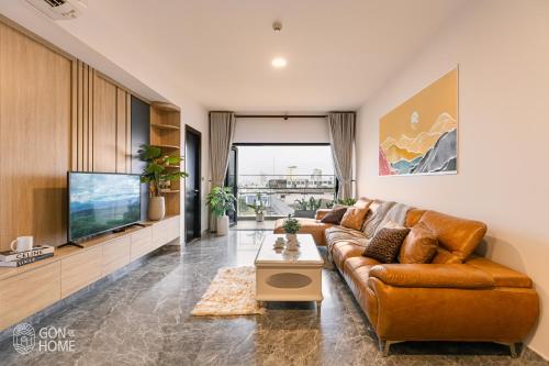 a living room with a brown leather couch and a tv at Luxury 2 or 3BR Apartment in Dist 1, Pool and airport pickup in Ho Chi Minh City