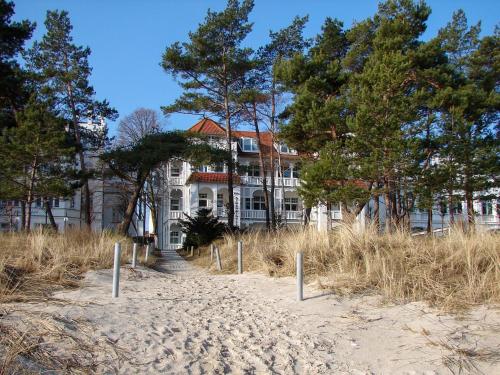 une grande maison blanche avec des arbres en face d'une plage dans l'établissement Villa Strandidyll Apartment 15, Meerblick, inkl Strandkorb, à Binz