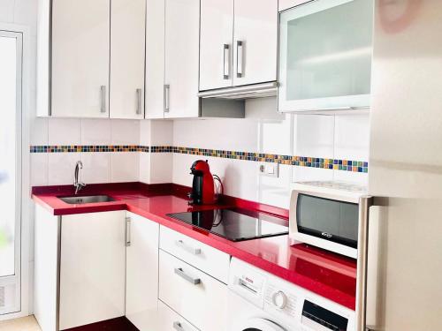 a white kitchen with a red counter top at Apartamento Romanilla Roquetas in Roquetas de Mar