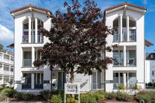 Un edificio blanco con un árbol delante. en Villa Strandidyll Neubau Ferienwohnung E4, en Binz
