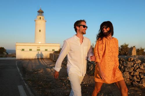 a man and a woman walking in front of a lighthouse at Hotel Riu Palace La Mola in Playa Migjorn