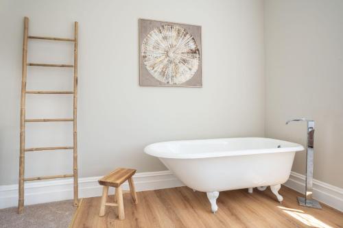 a bathroom with a white bath tub and a wooden stool at Country Retreat Sleeping 15 - Bron Menai in Newborough