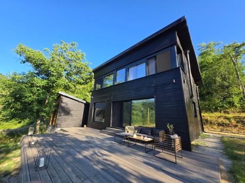 a black house on a wooden deck with chairs at Blackberry Cabin lakeside escape in Tubravić