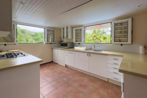 a kitchen with white cabinets and two windows at La Kaz Denel - 10min de La Trinité in Gros-Morne