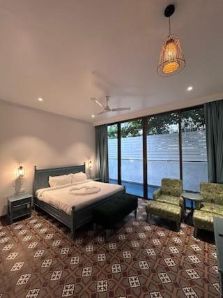 a bedroom with a bed and a chair and windows at Dia Hotels and Homes Nerul Goa - Villas and Apartments in Nerul