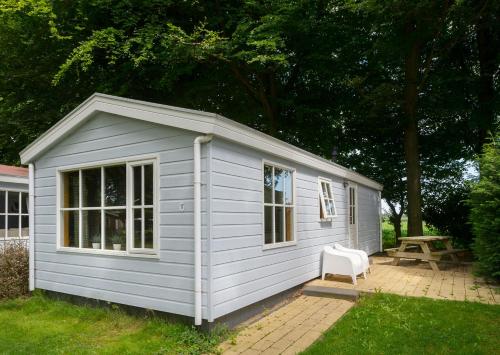 a small white shed with a chair in a yard at Camping Mareveld in Schimmert