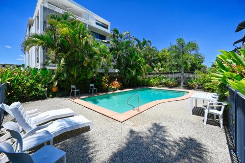 a swimming pool with white chairs next to a building at Luxe Coastal Escape, Sunny Coast in Maroochydore