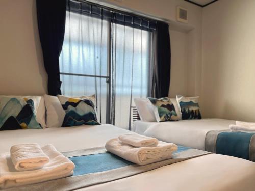 two beds with towels on them in a room with a window at nestay house osaka imazato in Osaka