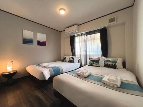 two beds in a small room with a window at nestay house osaka imazato in Osaka