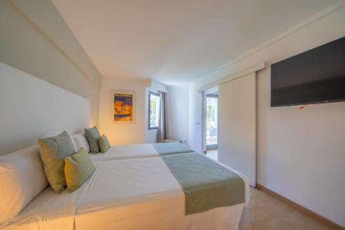 a white bedroom with a large bed and a flat screen tv at Playa Esperanza Resort Affiliated by Meliá in Playa de Muro
