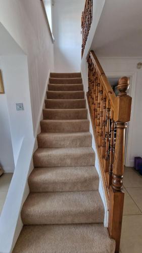 a staircase with brown carpeting and a wooden stair case at SnoozeDen Westmead - Windsor Castle & Legoland in Windsor