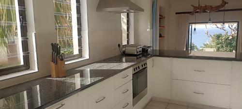 una cocina con armarios blancos, fregadero y ventanas en Beach & Golf Escape, en Southbroom